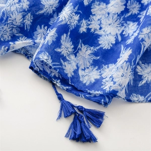 Détail d'une écharpe bleue légère avec imprimé floral et glands à franges assortis