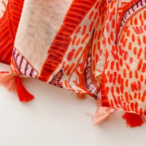 Close-up of lightweight linen-feel scarf with orange leaf patterns and fringe tassels