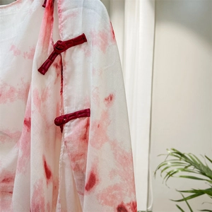 Detail of red traditional frog buttons and ink-wash pattern on white cotton scarf
