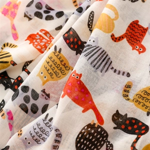 Close-up of soft cotton muslin fabric with colorful cartoon cat print and woven texture