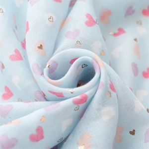Detailed close-up of light blue cotton scarf fabric with golden heart foil print