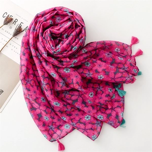 Detail of rose pink scarf with floral prints and colorful tassels on a minimalist desk