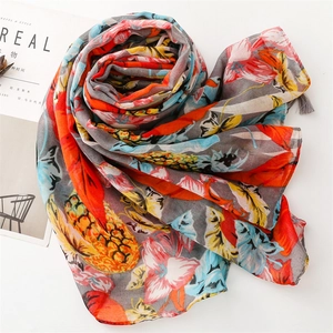 Close-up of vibrant fruit print scarf with gray fringe tassels and lightweight fabric