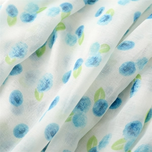 Detailed close-up of thin white scarf fabric with blue berry and green leaf print patterns