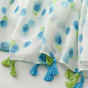 Detail of white summer scarf showing blue blueberry print and colorful fringe tassels