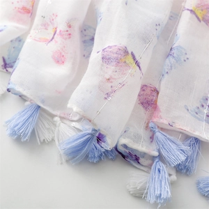Detailed macro view of watercolor butterfly prints and blue fringe tassels on a white scarf