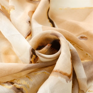 Macro view of beige scarf featuring golden foil accents and abstract ink wash patterns