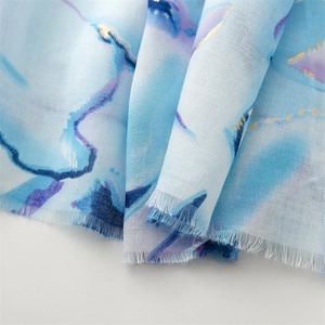 Close-up of gold foil floral print on blue marble pattern scarf with frayed edges