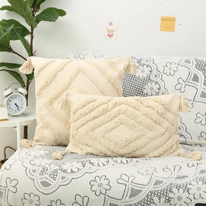 Boho beige tufted throw pillow with geometric patterns and tassel accents on sofa