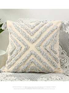 Detail of bohemian tufted geometric texture and grey corner tassels on cream pillowcase