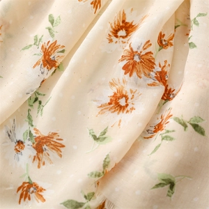 Macro detail of beige cotton linen scarf featuring orange daisies and golden foil dots