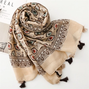 Détail d'une écharpe beige aspect lin avec motifs de fleurs et finitions à pompons
