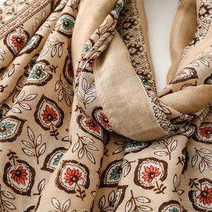 Détail d'une écharpe bohème à fleurs avec motifs de feuilles et glands sur fond blanc
