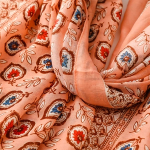 Gros plan sur une écharpe bohème pêche avec motifs floraux, bordures à franges et texture douce