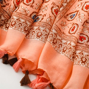 Détail d'écharpe en lin corail avec motifs floraux ethniques et pompons bicolores délicats