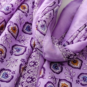 Gros plan sur l'imprimé fleuri bohème et les glands d'un châle en coton et lin mauve