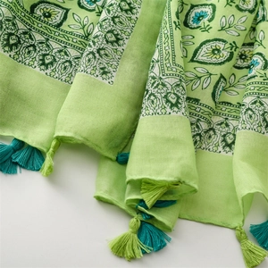 Vue détaillée d'une écharpe en coton vert clair avec motifs floraux et pompons bicolores