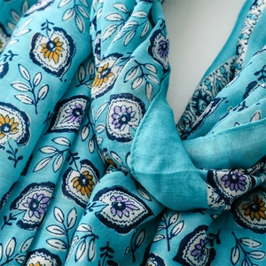 Détail d'une écharpe bleue en coton et lin avec feuilles blanches et motifs floraux
