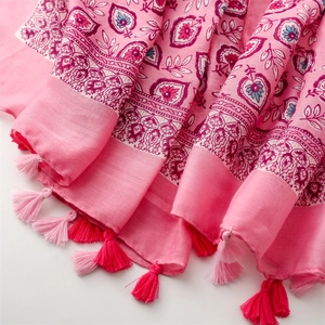 Détail d'une écharpe rose en lin avec des motifs bohèmes et des finitions à pompons