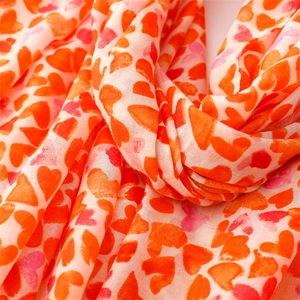 Gros plan d'une écharpe légère en coton et lin avec imprimés de cœurs orange et rose