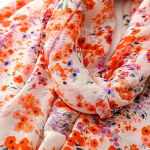 Gros plan du motif floral sur une écharpe beige légère aux fleurs orange et violettes