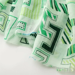 Detail of light green linen-feel scarf featuring dark geometric patterns and frayed edges