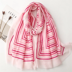 Pink striped cotton linen scarf with frayed edges displayed on a minimalist white desk