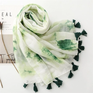 Détail d'une écharpe tie-dye vert et blanc avec pompons et texture de tissu léger