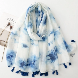 Détail d'une écharpe légère tie-dye blanc et bleu avec des pompons à franges denses