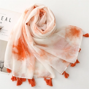 Gros plan sur l'écharpe tie-dye orange avec pompons détaillés et texture légère