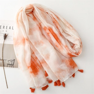 Vue détaillée d'une écharpe tie-dye orange et blanche avec franges sur une table épurée