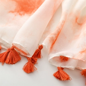 Détail d'une écharpe dégradée avec pompons orange et texture légère et respirante