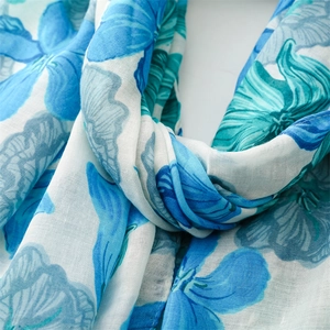 Detailed close-up of blue floral cotton-linen texture and tassel fringe on a light scarf