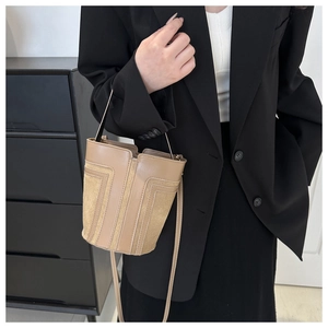 Dettaglio della borsa a secchiello kaki con texture in pelle liscia e glitterata sulla modella