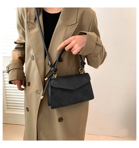 Detail of black crossbody bag featuring rope knot handle and golden metal ring accents