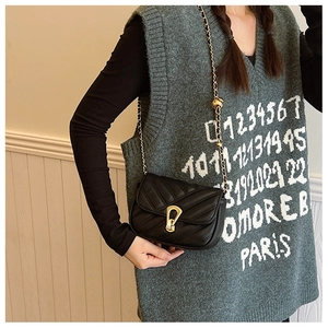 Détail d'un sac bandoulière noir matelassé en chevron avec boucle dorée et bandoulière chaîne