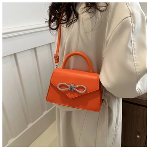 Detail van een feloranje crossbodytas met een sprankelende gesp van strass-strik