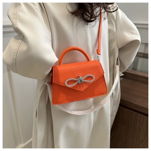 Detail van helder oranje handtas met een fonkelende strass-strik en glad PU-kunstleer