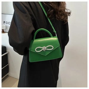 Model wearing vibrant green handbag with rhinestone bow and crossbody strap over black blazer