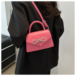 Detail van een felroze handtas met een sprankelende strass-strik op een zwarte blazer