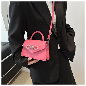 Detail van roze handtas met strass-strik gedragen door een model in zwarte kleding