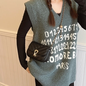 Quilted black crossbody bag with gold chain strap and metal clasp on green vest model