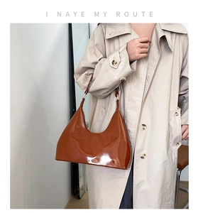 Detail of glossy brown patent leather hobo bag with adjustable strap and gold hardware