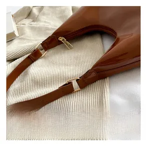 Detail of gold metal hardware and brown glossy patent leather on shoulder bag