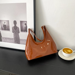 Glossy caramel patent leather underarm bag in minimalist crescent shape with gold buckle