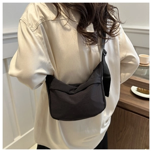 Detailed view of a minimalist black nylon crossbody bag worn by a model in a lifestyle setting