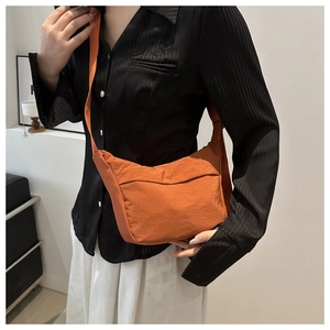 Detail of a bright orange nylon crescent crossbody bag worn with a black casual shirt