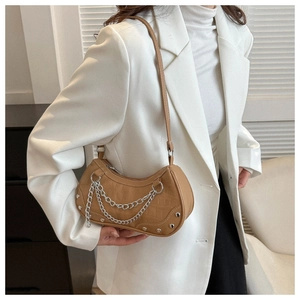 Detail of khaki crocodile pattern shoulder bag with silver chains and rivets on a white blazer