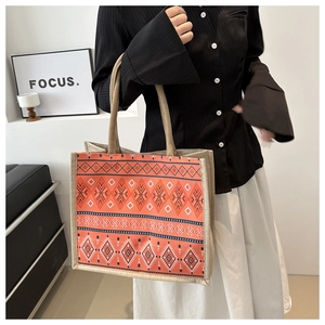 Detailed view of orange ethnic tote bag with black geometric patterns and woven handles