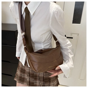 Brown PU leather crescent bag with wide geometric strap worn by model in casual style